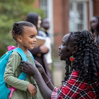 African American mothering helping her daughter put on her backpack