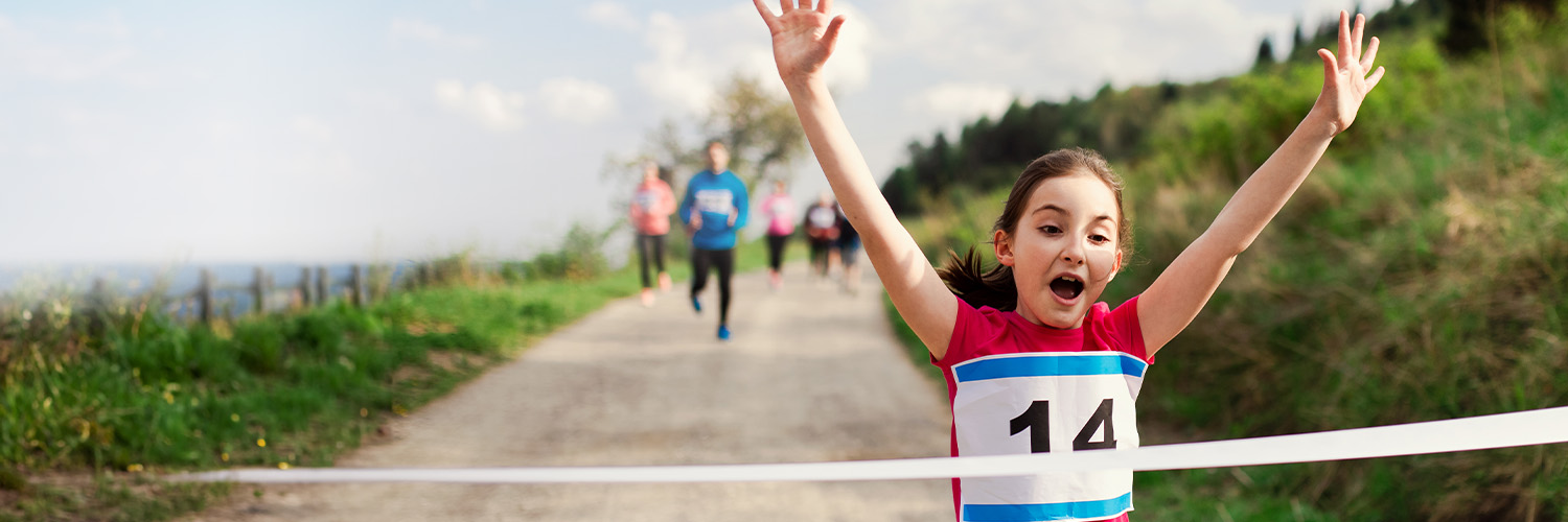 Young girl running through the finish line at a race.